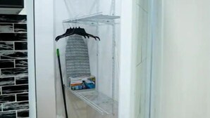 A narrow hallway with a tiled floor, a broom, a mop, and a metal shelf unit with a hanging rack. - Lovalier Luxury Studio (Fajardo)