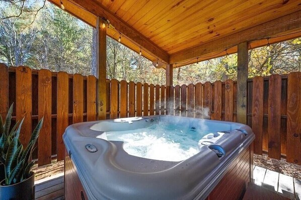 Un bain à remous installé sous une pergola en bois, le tout entouré d’une clôture en bois.
