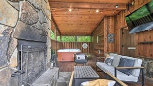 A cozy outdoor seating area with a stone fireplace, a hot tub, and a wooden deck. - Romantic-Back to School Get Away-Luxury-Private Location (Broken Bow)
