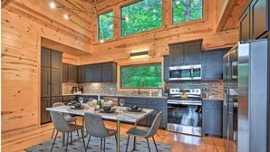 A modern kitchen with wooden walls, a stone backsplash, and a dining area with a table and chairs. - Romantic-Back to School Get Away-Luxury-Private Location (Broken Bow)