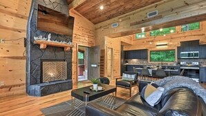 A spacious living area with a stone fireplace, wooden walls, a dining area, and a kitchen. - Romantic-Back to School Get Away-Luxury-Private Location (Broken Bow)