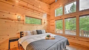 A wooden cabin bedroom with a bed, a nightstand, and a window overlooking greenery. - Romantic-Back to School Get Away-Luxury-Private Location (Broken Bow)