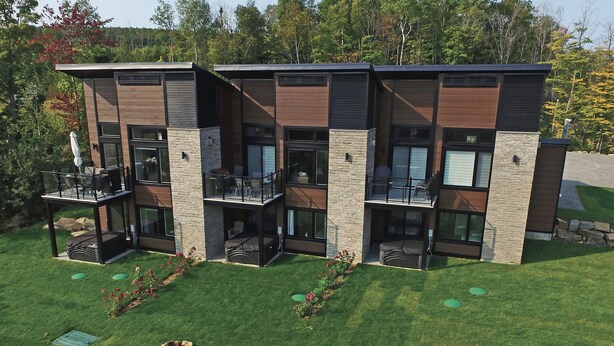 A modern multi-story building with balconies, large windows, and a well-maintained lawn. - Luxury mountain condo with golf and slide views (Saint-Jean-de-Matha)