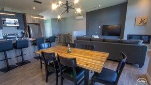 A modern kitchen with a dining area, a sofa, and a TV in a living room. - Luxury mountain condo with golf and slide views (Saint-Jean-de-Matha)