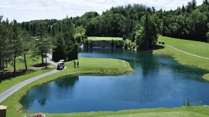 A golf course with a pond, a bridge, and a forested area. - Luxury mountain condo with golf and slide views (Saint-Jean-de-Matha)