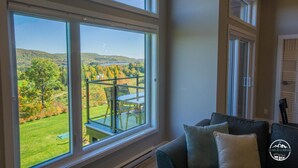 A room with large windows offering a view of a green landscape and hills. - Luxury mountain condo with golf and slide views (Saint-Jean-de-Matha)