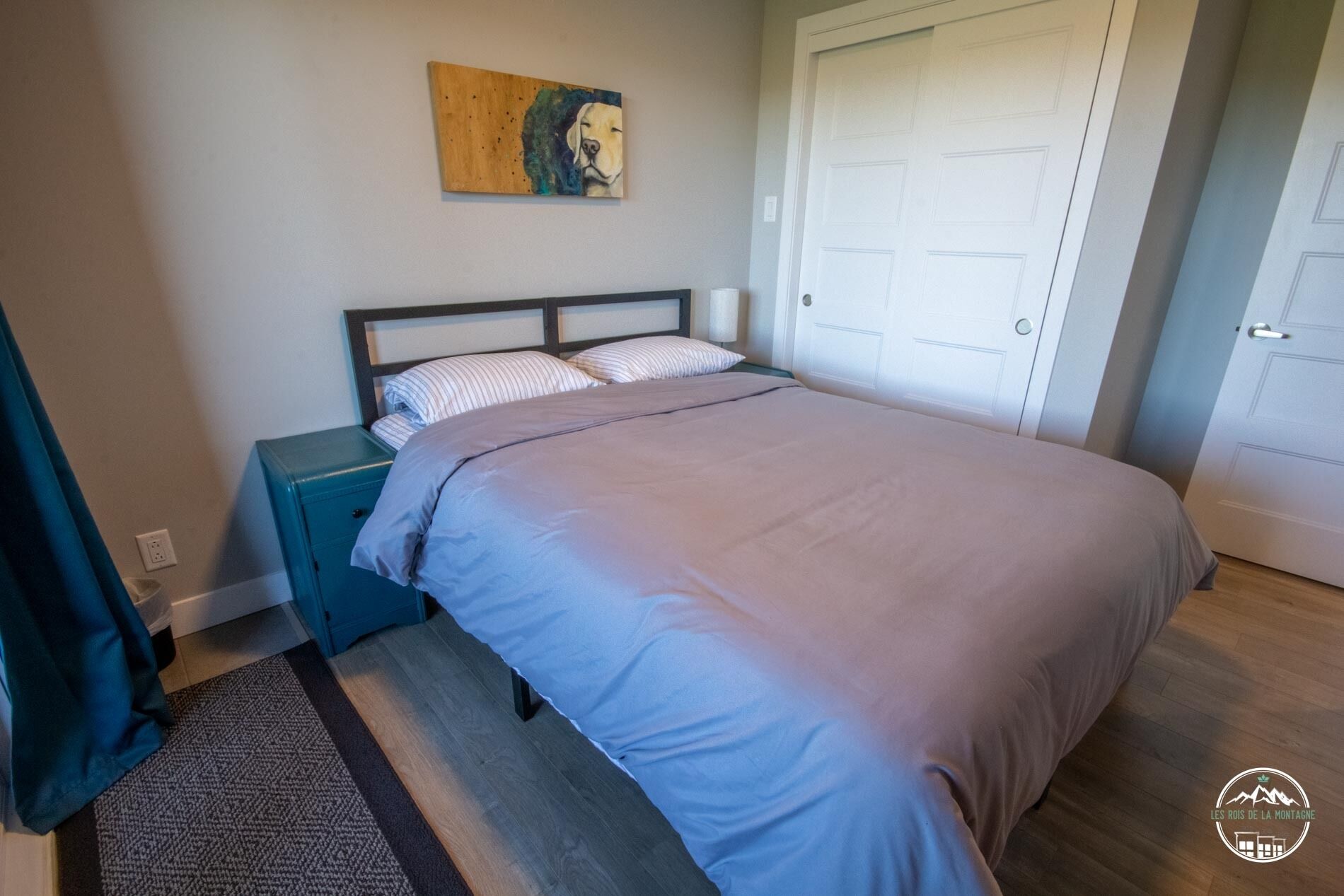 A bedroom with a bed, a nightstand, a painting on the wall, and a door.
