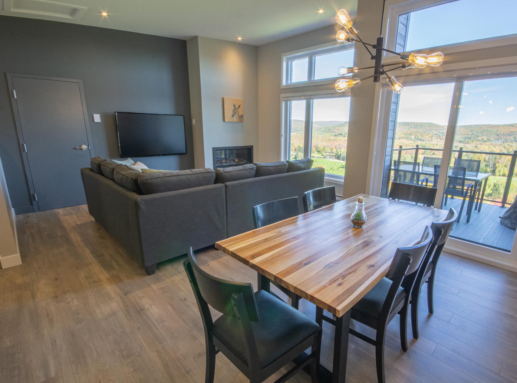 Un espacio habitable moderno con una mesa de comedor de madera, sofás grises, un televisor de pantalla plana y una chimenea.