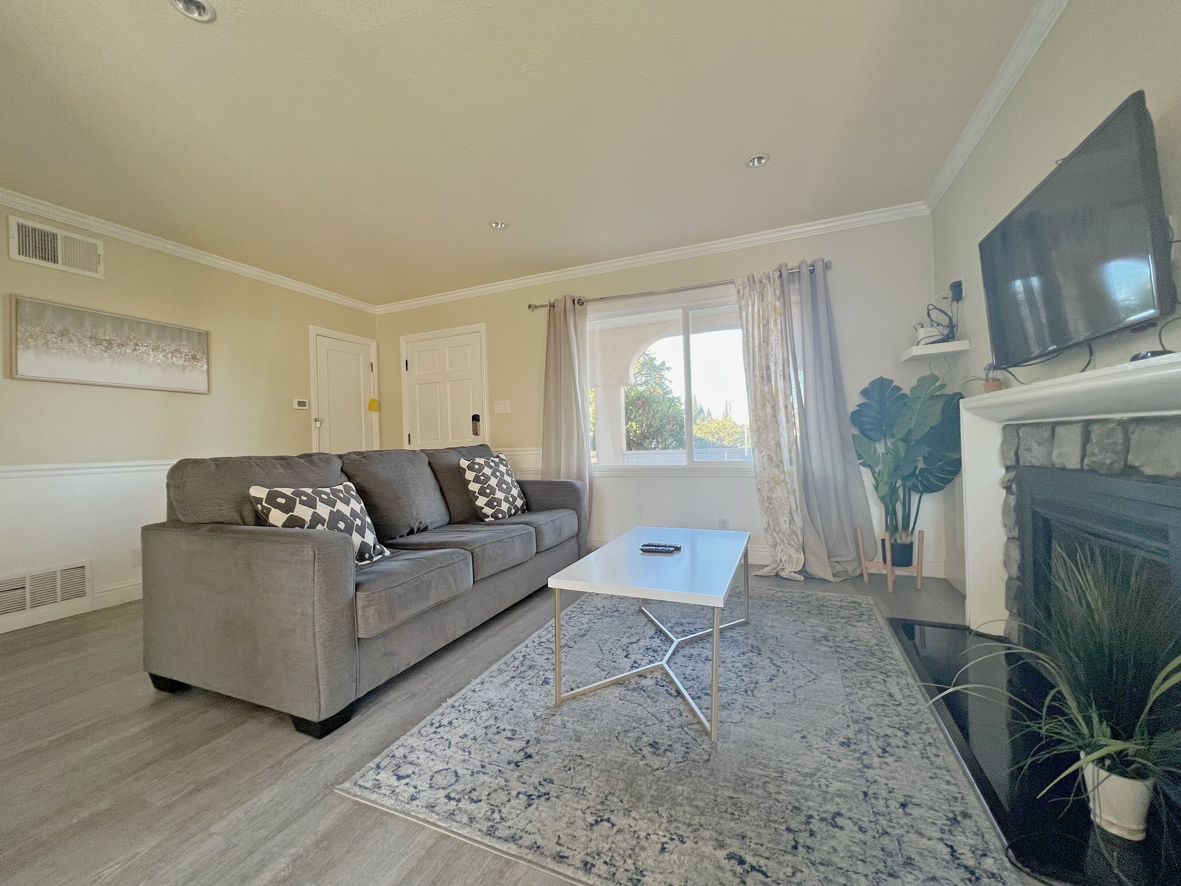A living room with a grey sofa, a white coffee table, a patterned rug, a fireplace, and a TV mounted on the wall.