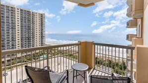 A balcony with a view of the ocean, a pool, and adjacent high-rise buildings.