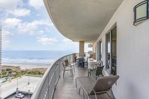 A balcony with a view of the ocean, outdoor furniture, and a pool area.