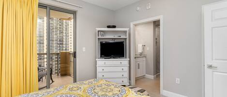 A bedroom with a bed, a TV, a wardrobe, and a bathroom visible through an open door.