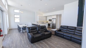 A modern living room with leather sofas, a dining area with a white table, and a kitchen with stainless steel appliances.