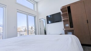 A bedroom with a large bed, a TV mounted on the wall, and a view of a snowy landscape through the windows.