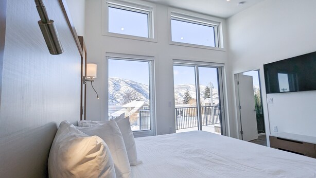 A bedroom with a large bed, multiple windows, and a view of snow-covered mountains.