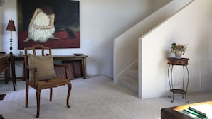 Un salon spacieux agrémenté d’un grand tableau, d’une chaise en bois, d’une lampe et d’un escalier.