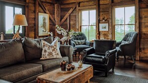 A rustic wooden interior with a sofa, armchairs, a coffee table, and framed artwork. - Kingdom Carriage House, Historic Home on 35 Acres in the Northeast Kingdom (Sutton)