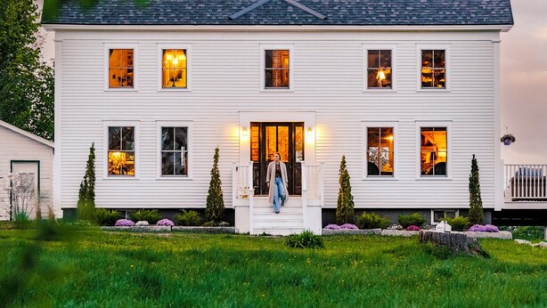 A two-story white house with a dark roof, multiple windows, and a front porch with steps. - Kingdom Carriage House, Historic Home on 35 Acres in the Northeast Kingdom (Sutton)
