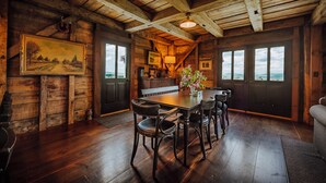 A rustic wooden interior with a dining table, chairs, a bench, and a view through the windows. - Kingdom Carriage House, Historic Home on 35 Acres in the Northeast Kingdom (Sutton)