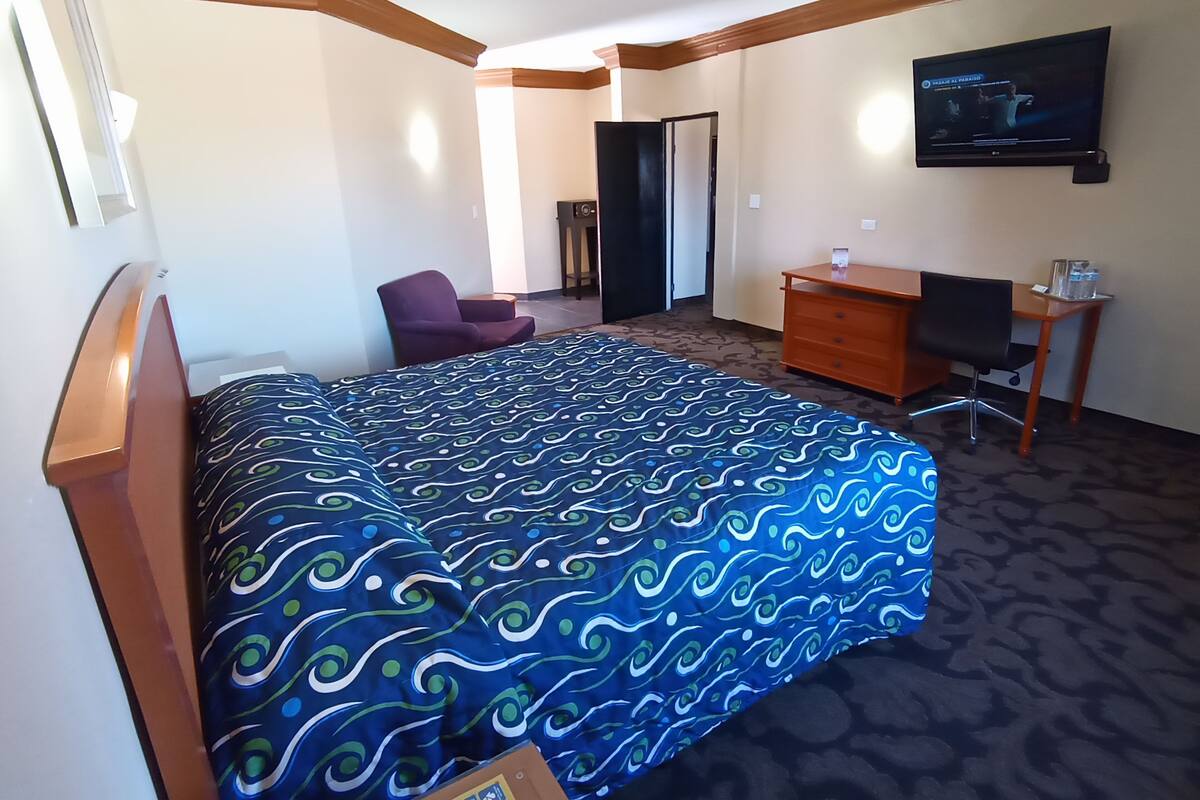 Una habitación de hotel con cama, escritorio, silla, televisión y puerta.