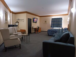 Ein Hotelzimmer mit einer Couch, einem Sessel, einem Schreibtisch, einem Fernseher und einem Bett.
