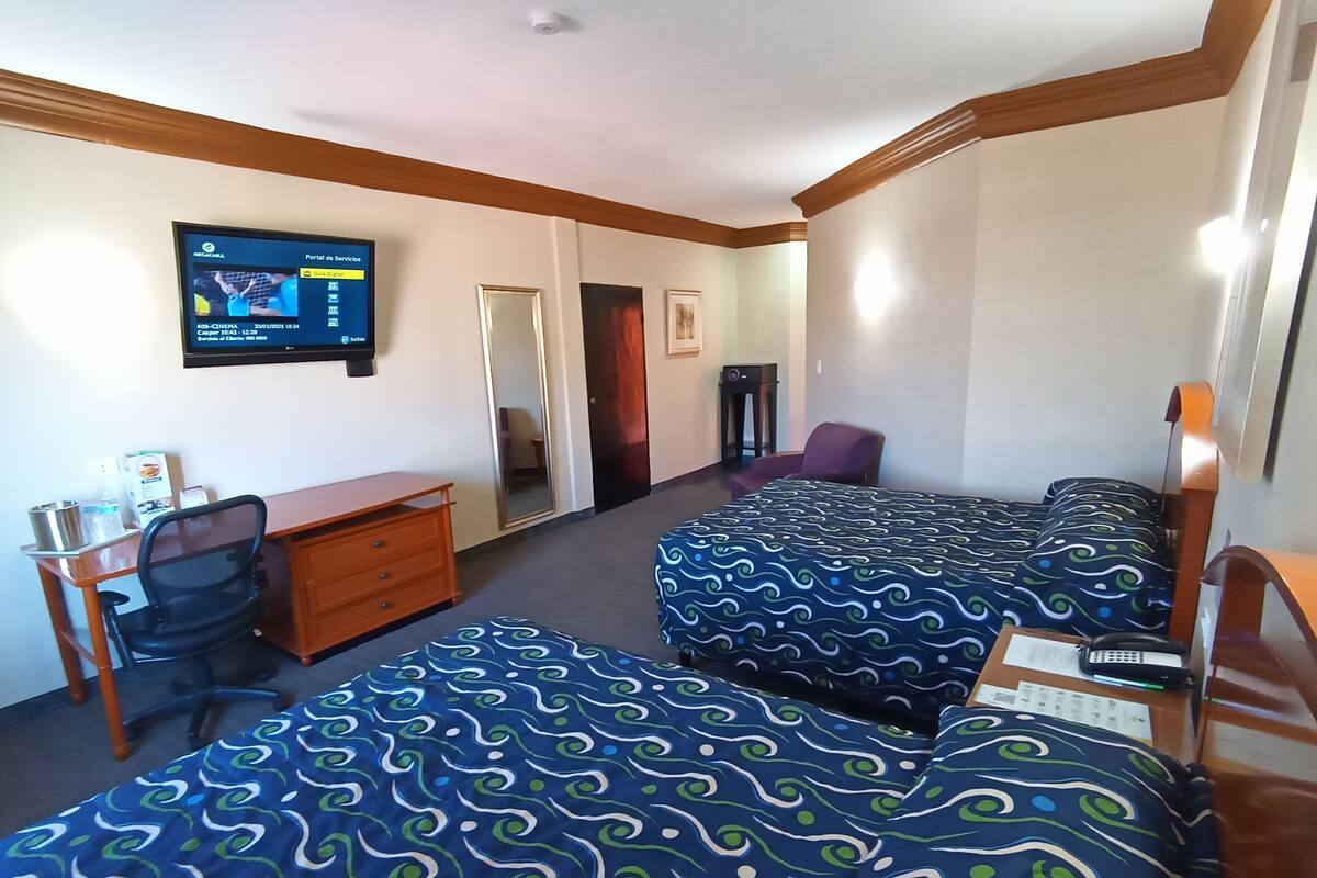 Una habitación de hotel con dos camas, un escritorio, una silla, un televisor y un espejo.