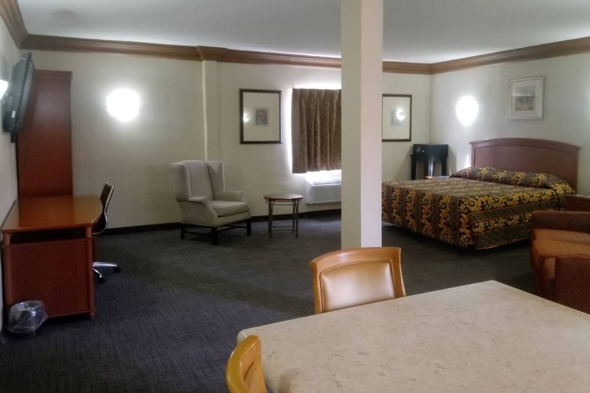 Una habitación de hotel con una cama, un escritorio, una silla, una mesita y una ventana con cortinas.