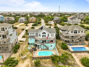 A coastal residential area with multiple two-story houses, a central swimming pool, and a view of the ocean. - 8BR Oceanfront home - Game & theater rooms, private pool, hot tub ★★★★★ (Waves)