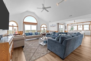 A spacious living area with a large sofa, a coffee table, and a TV. There are arched windows and a ceiling fan.