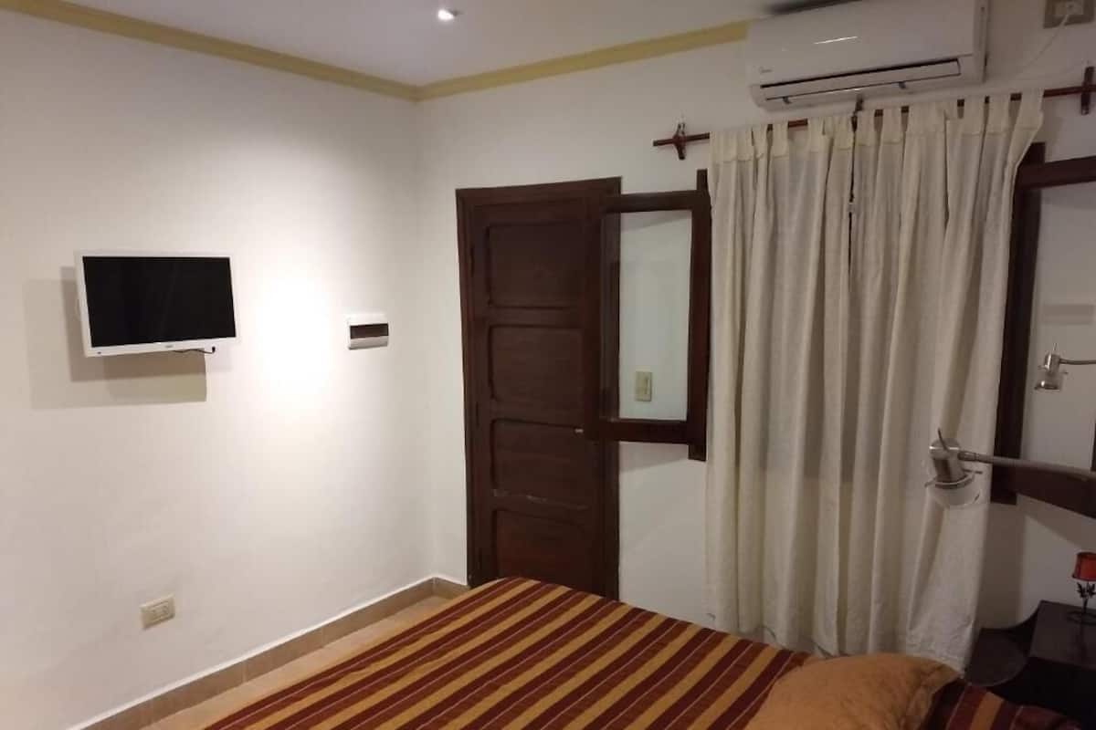 Quarto com cama, televisão, ar condicionado, porta e cortina.