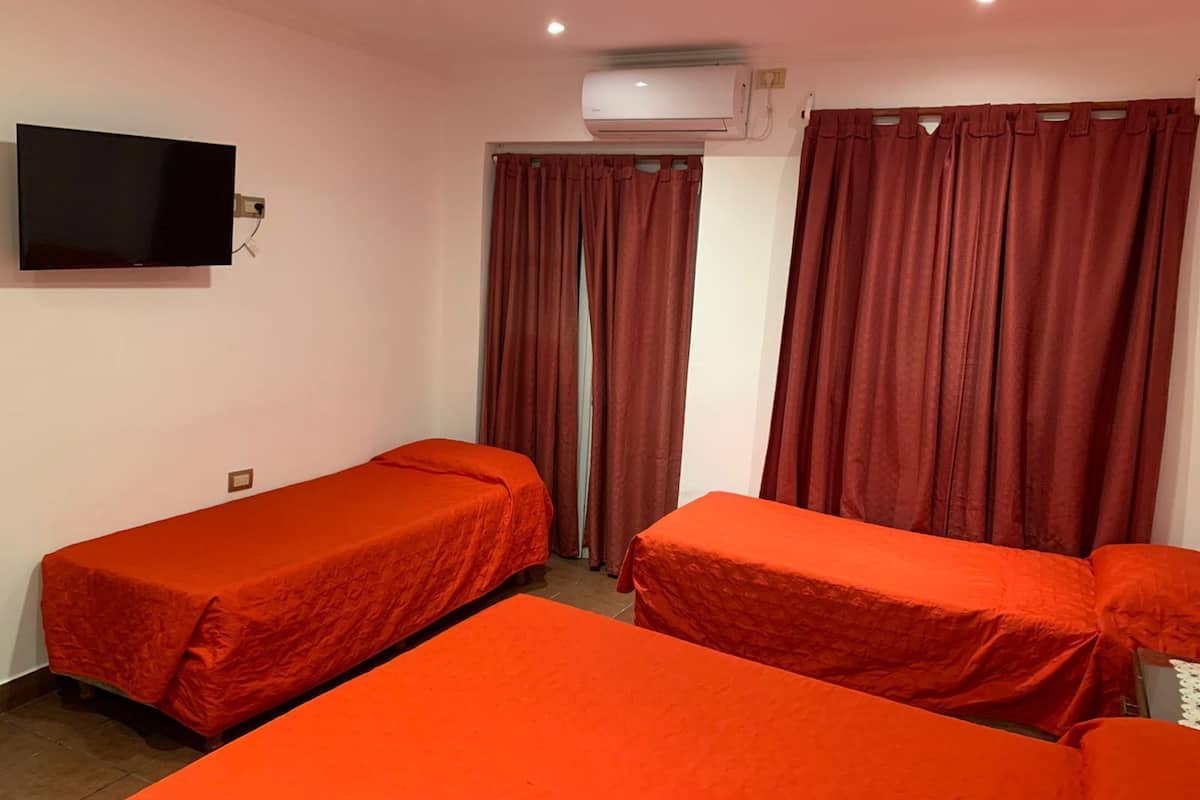 Quarto com duas camas de solteiro, televisão de tela plana, ar condicionado e cortinas vermelhas.