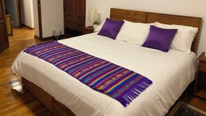 Un lit bien fait, avec une couverture colorée, deux oreillers violets et une tête de lit en bois.
