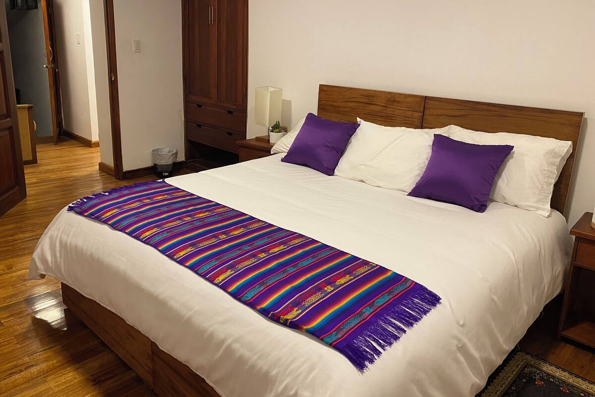 A neatly made bed with a colorful blanket, two purple pillows, and a wooden headboard.