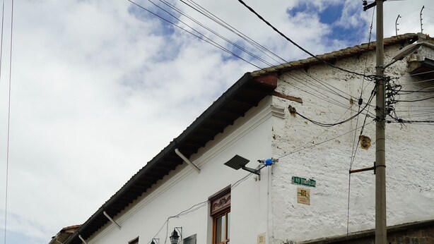 A white building with a stone base, a staircase leading up to the entrance, and a flag hanging outside. - Casa Francisco Hotel (Quito)