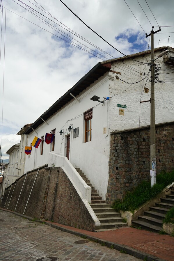 Un edificio blanco con base de piedra, una escalera que conduce a la entrada y una bandera colgada afuera.