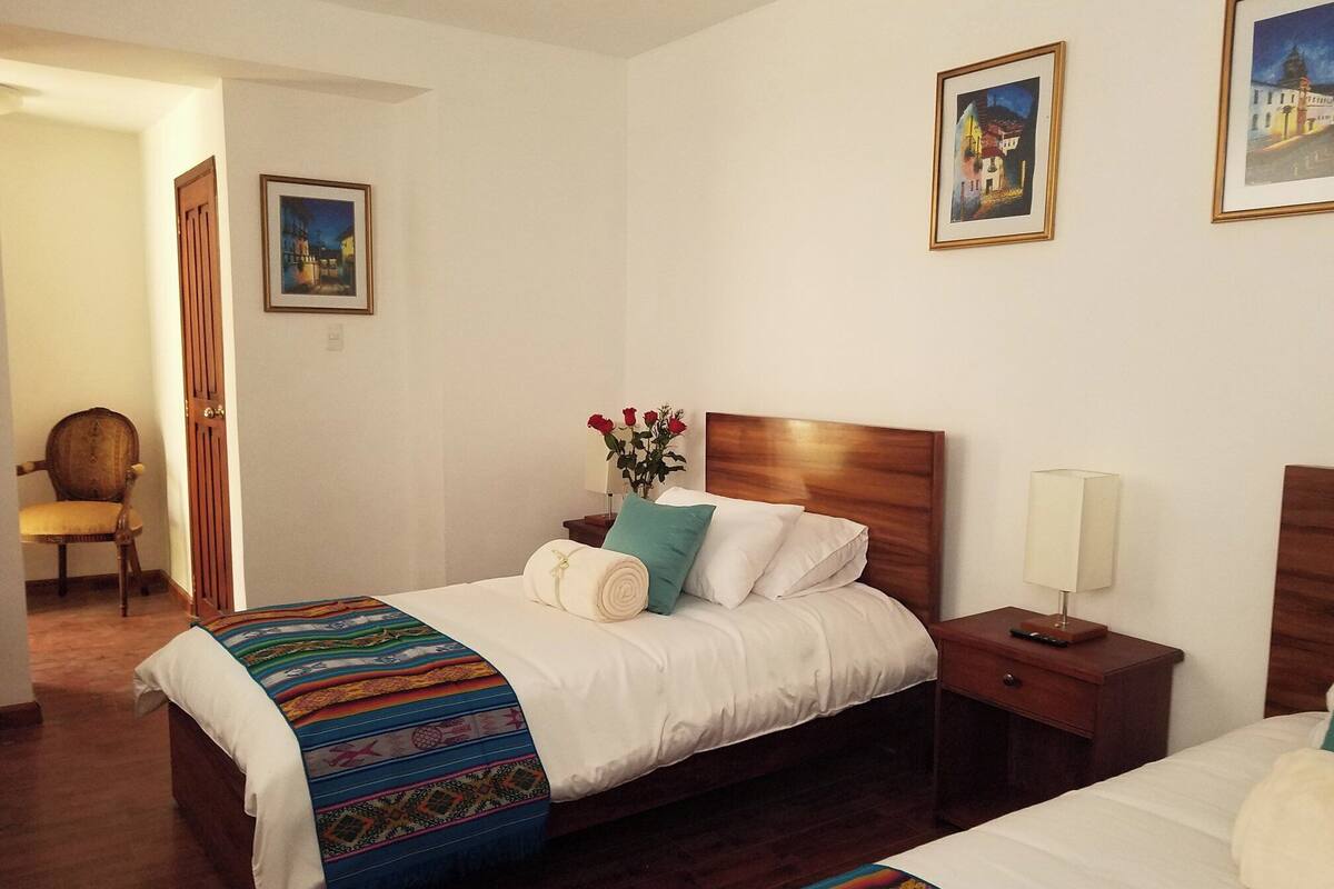 A hotel room with a wooden bed, a nightstand with a lamp, a chair, and two framed pictures on the wall.