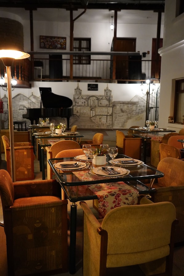 Un espace repas avec des tables dressées pour le repas, des chaises et un piano en arrière-plan.