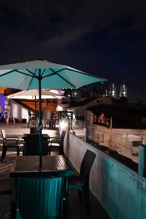 An outdoor seating area with tables and chairs, a large umbrella, and a view of buildings in the background. - Casa Francisco Hotel (Quito)