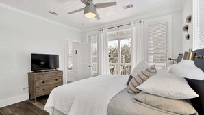 Een slaapkamer met een bed, een televisie op een houten dressoir en een plafondventilator.