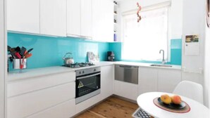 A compact kitchen with white cabinets, a blue countertop, a stove, a dishwasher, and a small table with fruit. - Bondi local garden living, 5 mins walk to beach (Bondi Beach)