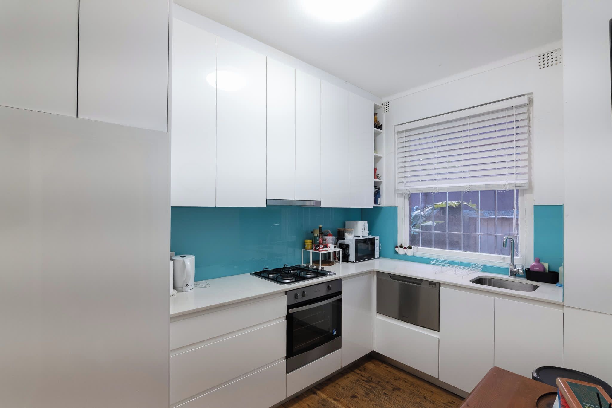 A compact kitchen with white cabinets, a gas stove, an oven, a microwave, and a window with blinds.