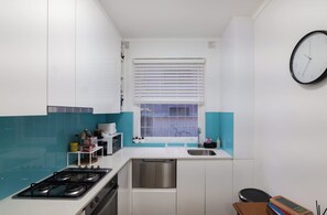 A compact kitchen with white cabinets, a stainless steel dishwasher, a gas stove, and a window with blinds.