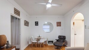 A living room with a ceiling fan, a round mirror, a dining table with chairs, a black leather chair, a white sofa, and a red patterned rug. - Bondi local garden living, 5 mins walk to beach (Bondi Beach)