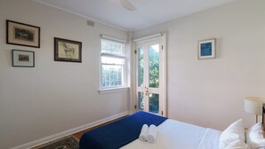 A bedroom with a bed, a ceiling fan, a window, and framed pictures on the wall. - Bondi local garden living, 5 mins walk to beach (Bondi Beach)