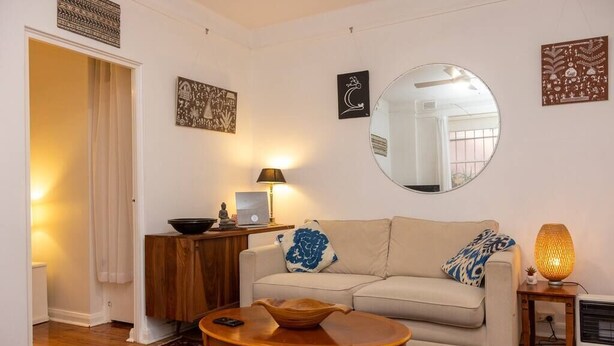 A living room with a sofa, a round coffee table, a mirror, and a lamp. - Bondi local garden living, 5 mins walk to beach (Bondi Beach)