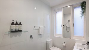 A modern bathroom with a glass shower enclosure, a toilet, a sink, and a shelf with toiletries. - Bondi local garden living, 5 mins walk to beach (Bondi Beach)