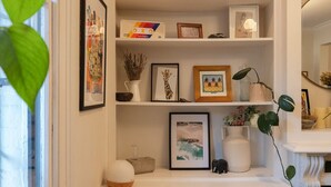 Un mobile sospeso bianco con ripiani che ospitano quadri incorniciati, un piccolo vaso e una pianta decorativa.