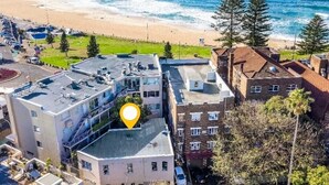 An aerial view of a coastal area with a building marked by a location pin, adjacent to a beach and ocean. - Incredible Beachside Location 4 Bed Apartment (Bondi Beach)