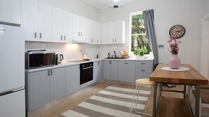 A modern kitchen with white cabinets, a microwave, a coffee maker, and a wooden dining table with a vase of flowers. - Incredible Beachside Location 4 Bed Apartment (Bondi Beach)