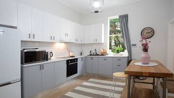 A modern kitchen with white cabinets, a microwave, a coffee maker, and a wooden dining table with a vase of flowers.